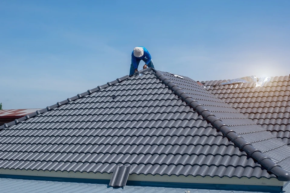 Ouvrier de couverture en vêtements et gants de protection spéciaux, à l'aide d'un pistolet pneumatique et à l'installation de tuiles de toit en béton sur le nouveau toit, Concept de bâtiment résidentiel en construction