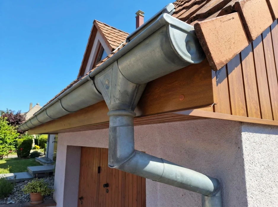 Gouttière semi-ronde en zinc patiné fixée à l'avant-toit d'une maison individuelle