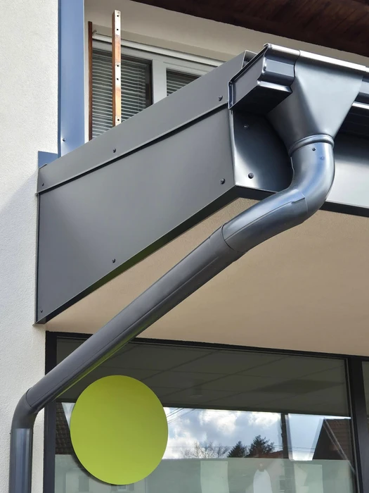 Façade extérieure d'un bâtiment commercial avec installation neuve de gouttière et descente pluviale en zinc prépatiné anthracite RAL 7016