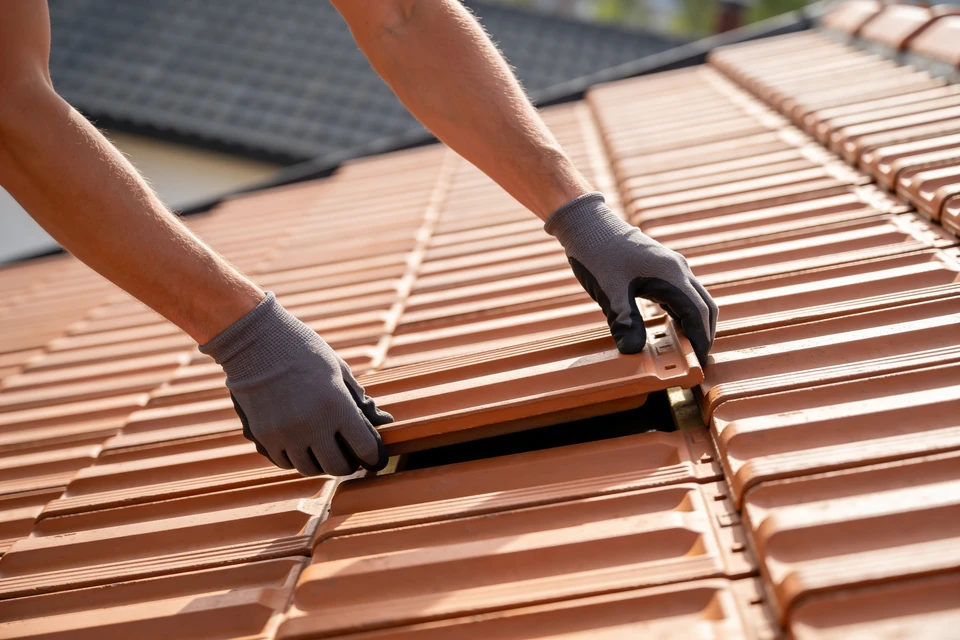 Vue d'une maison avec toiture en tuiles ou ardoise, l&eacute;g&egrave;rement endommag&eacute;e ou n&eacute;cessitant des travaux, prise de l'ext&eacute;rieur en lumi&egrave;re naturelle. Au premier plan, une personne en tenue professionnelle (artisan ou client) et un professionnel en &eacute;quipement de s&eacute;curit&eacute; discutent devant la maison, tenant des documents ou un devis. L'atmosph&egrave;re doit transmettre la confiance, la facilit&eacute; d'acc&egrave;s aux solutions de financement et la collaboration constructive entre le professionnel et son client.