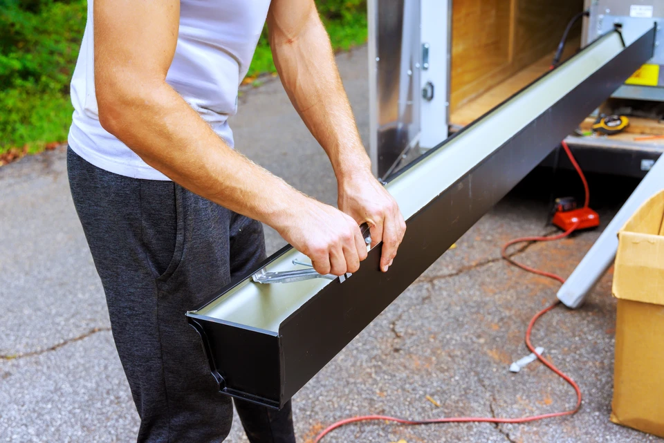 Deux couvreurs travaillent sur une toiture en pente, installant des liteaux métalliques